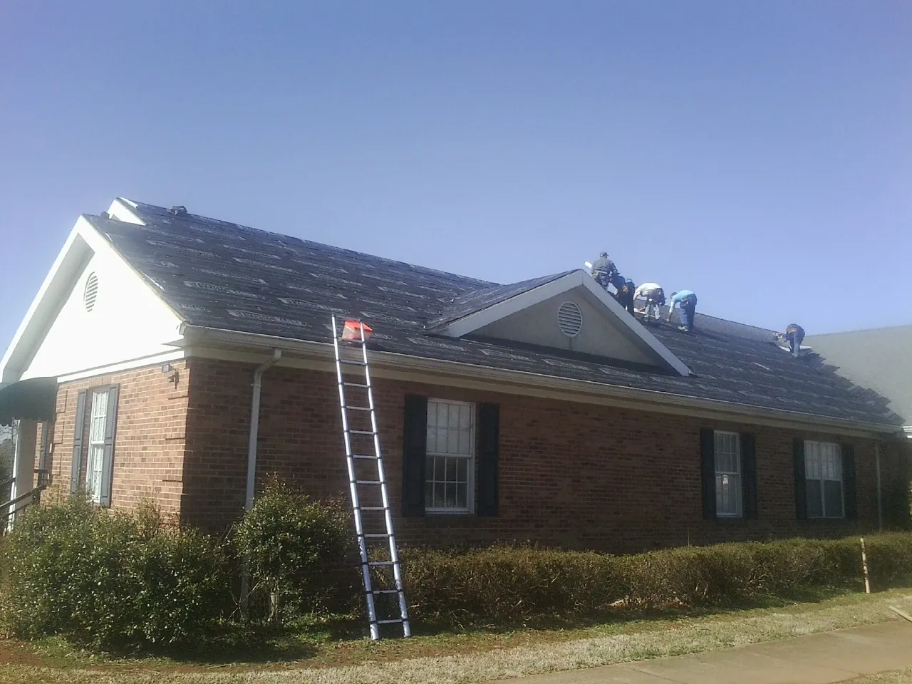 Crew tearing shingles off a brick ranch roof with a ladder set — Emergency Roof Repair work by our crew in Imogene