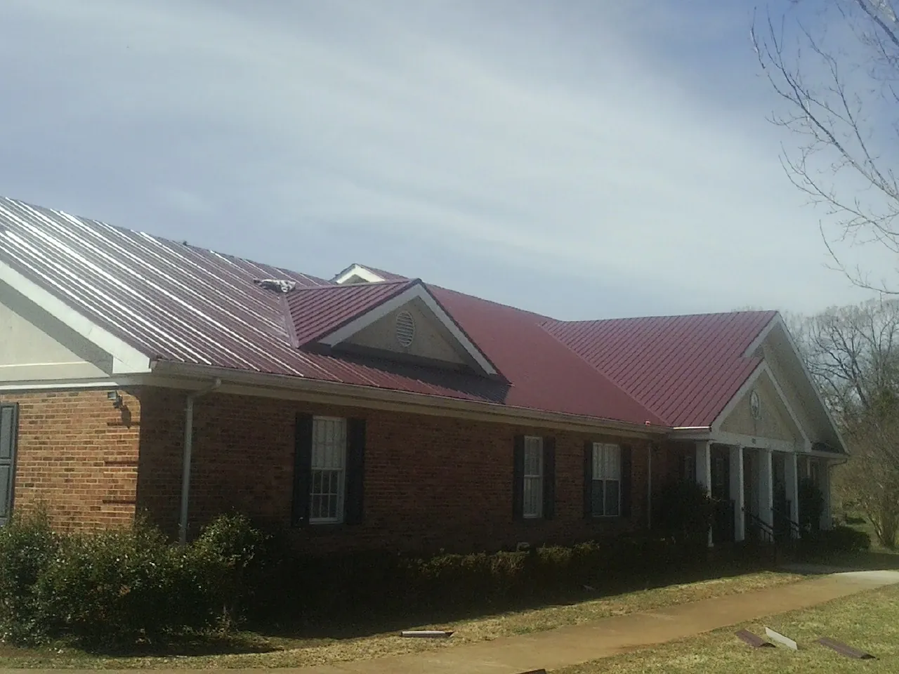 Red metal roof with gabled entries on a long brick building, from a Hail Damage Roof Repair job in Imogene