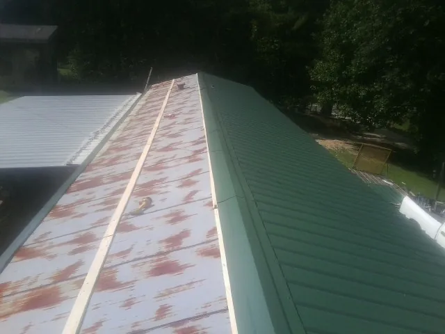 Old rusted panels beside newly installed green metal roofing — Wind Damage Roof Repair by Roofing Brothers in Imogene