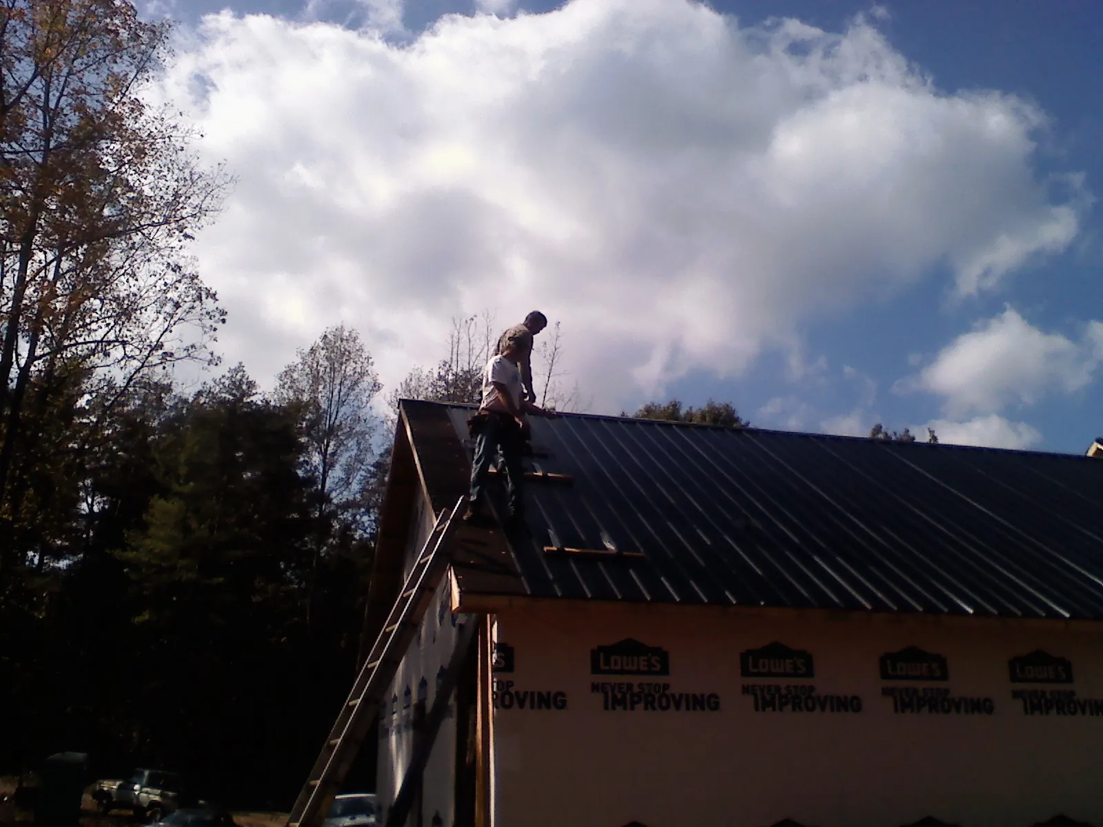 Roofer fastening dark metal panels high against a cloudy sky, from a Roof Inspection job in Imogene