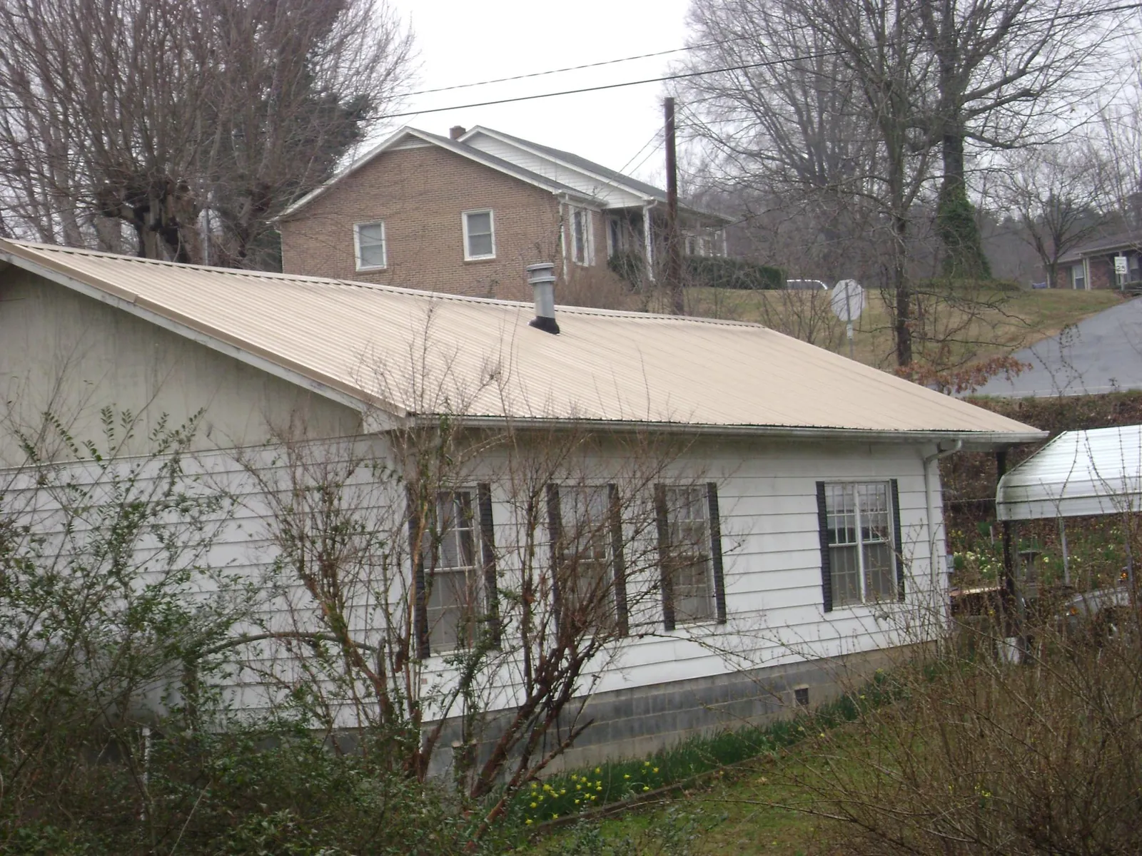 Tan metal roof on a white sided house set into a hillside — Commercial Roofing by Roofing Brothers in Imogene